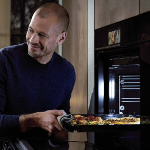 Einbauküche mit modernem Backofen, Mann holt frische Pizza aus dem Ofen und sorgt für eine gemütliche Kochatmosphäre